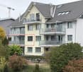 Modern multi-story residential building with multiple balconies, large windows, and a well-maintained garden area.