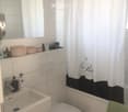 Modern bathroom with white tiles, a sink with a faucet, a toilet, a mirror above the sink, a shower curtain, and various toiletries on the cabinet.