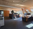 Office space with wooden ceiling, desks, chairs, computers, printers, cabinets, and plants.