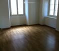 Empty room with wooden flooring, white walls, and two windows allowing natural light to enter.