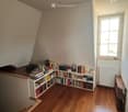 A cozy attic room with wooden floors, a large window, a bookshelf filled with books, and a small table near the window.