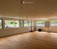 Bright, unfurnished room with wooden flooring, large windows, and minimal furniture including a table, chairs, a ball, and a screen.