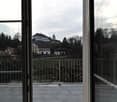 Balcony with a metal railing, tiled floor, and a scenic view of a town with buildings and trees.
