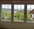 A room with large windows offering a scenic view of a lake and surrounding greenery, featuring a small glass table near the windows.