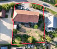 Aerial view of a two-story house with a tiled roof, surrounded by a garden and driveway with multiple parked cars.