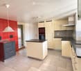 Modern kitchen with light-colored cabinets, black countertops, stainless steel sink, and a red tiled accent wall.