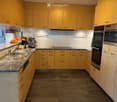 Modern kitchen with light yellow cabinets, granite countertops, stainless steel appliances, and a fruit bowl on the counter.