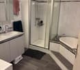 Modern bathroom with a bathtub, shower, sink, and mirror. Features tiled walls, a dark floor, and a glass-enclosed shower area.