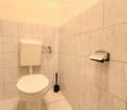 A small bathroom with white tiled walls, a toilet, and a toilet brush.