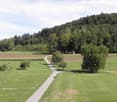 A peaceful rural landscape with green fields, a winding road, scattered trees, and a small building in the distance.