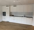 Empty kitchen with white cabinets, a sink, and a wooden floor. No furniture or appliances are present.