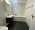 Modern bathroom with white tiles, black floor, sink, bathtub, toilet, and mirror.