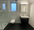 Modern bathroom with white tiles, black floor, glass-enclosed shower, toilet, sink with mirror, and built-in cabinet.