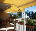 Balcony with a yellow retractable awning, several potted plants, and a small dining set with chairs and a table.