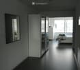 Modern, minimalist bedroom with dark flooring, large mirror, sliding wardrobe, and neatly made bed.