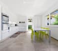 Modern kitchen with white cabinets, stainless steel oven, a dining table with green chairs, and a view of the garden through large windows.