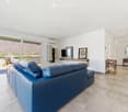 Modern living room with a blue leather sofa, a television mounted on the wall, a mirror, a small wooden table, and a chair near the balcony with a scenic mountain view.