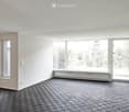 Empty room with light-colored walls, dark checkered flooring, large windows, and a sliding glass door leading outside.