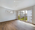Bright, unfurnished room with wooden flooring, large sliding glass doors leading to a balcony, and a small window on one wall.