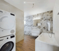 Modern bathroom with a bathtub, sink, mirror, and a private washing machine. The walls feature a decorative stone-patterned tile design, and the floor is made of polished wood.