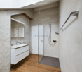 Modern bathroom with a white vanity, sink, mirror, and a glass-enclosed shower area. The walls are tiled, and the floor is wooden.