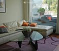 Modern living room with a white leather sofa, glass coffee table, and a view of the city and mountains through large windows.