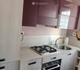 Modern kitchen with light wood cabinets, gas stove, sink, and built-in oven. Features a sleek design with a neutral color palette.