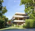 Modern two-story residential building with a clean, contemporary design, surrounded by lush greenery and trees.