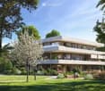 Modern multi-story residential building with balconies, surrounded by a well-maintained garden with trees and shrubs.