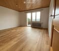 Empty room with wooden flooring, white walls, and a slanted wooden ceiling. Features a large window with a view and a radiator below it.