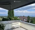 Balcony with a white bench, potted plants, and a retractable awning, overlooking a scenic landscape with trees and distant mountains.