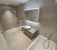 Modern bathroom with a sleek sink, mirror, toilet, bathtub, and glass-enclosed shower area.