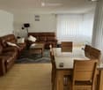 Living and dining area with a brown leather sofa, coffee table, dining table with chairs, and a floor lamp.