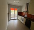Empty kitchen with white cabinets, a stove, sink, and a sliding glass door leading to a balcony.