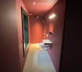 Modern bathroom with a toilet, sink, and shower. The walls are painted in a warm, reddish hue, and the floor is light-colored. The lighting is soft and warm, creating a cozy atmosphere.