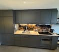 Modern kitchen with dark grey cabinets, wooden countertop, stainless steel sink, induction cooktop, and built-in oven. Features a decorative backsplash with a textured design.