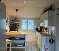Modern kitchen with white cabinets, a central island, and a sink area. Includes a stool, coffee maker, oven, and various kitchen utensils.