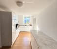 Modern kitchen with light-colored cabinets, a marble countertop, and wooden flooring. Features an oven, sink, and faucet.