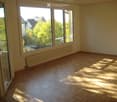 Empty room with wooden parquet flooring, large windows, and radiators. No furniture or equipment present.