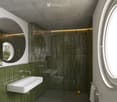 Modern bathroom with green tiled walls, a white sink, a large round mirror, a glass-enclosed shower, and a toilet. Features include built-in LED lighting and a small plant on the windowsill.