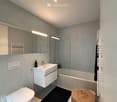 Modern bathroom with white tiles, a sink with a mirror, a toilet, a bathtub, a wicker basket, and a radiator.