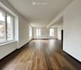 Empty room with wooden flooring, white walls, and large windows, featuring a slanted ceiling and multiple doorways.