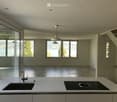 Modern kitchen with white countertops, a sink, faucet, and induction cooktop, large windows offering a scenic view of a lake and mountains.