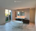 Modern bathroom with a freestanding bathtub, double sink vanity, large mirror, and sleek faucet. The space features large tiles and a sliding glass door leading to an outdoor area.