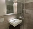 Modern bathroom with a white sink, dark wooden cabinet, large mirror, and glass-enclosed shower area.