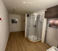 Bathroom with wooden flooring, white brick walls, a white sink, and a glass-enclosed shower stall.