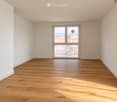 Empty room with light wooden flooring and white walls, featuring large windows and a door leading to a balcony.