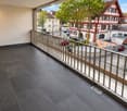 Balcony with dark tiled floor, metal railing, overlooking a street with houses, trees, and parked cars.