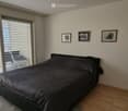Modern bedroom with a large window, a neatly made bed, a fan, and three picture frames on the wall.