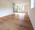 Empty room with wooden flooring, white walls, and large windows with a sliding glass door leading to a balcony.